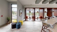 Located at 1989 Cheshire Bridge Rd NE in Atlanta's dynamic Cheshire Bridge neighborhood, this single-floor community space makes a striking first impression with its bold teal accent walls, large-format marble-look tile flooring, and an open, flowing layout that connects multiple functional zones seamlessly.

The main corridor draws visitors through vivid teal archways, with a reception-style counter near the entrance offering a welcoming workstation. A dramatic red sheer curtain acts as a design focal point and soft room divider, adding warmth and visual interest against the cool teal palette.

Floor-to-ceiling windows flood the lounge and seating areas with natural light, providing open views of the surrounding greenery and streetscape. Built-in wooden banquette booths with pendant globe lighting offer intimate nooks for conversation or work, while modular hexagonal ottomans in yellow, teal, and charcoal provide flexible, casual seating throughout.

Deeper within the space, an additional lounge and gathering area features patterned carpet, eclectic wall art, and ample seating configurations suited for both individual use and group interaction. A communal table with bar-height seating creates a collaborative work or social hub.

Throughout, the design balances energetic color with clean modern architecture, creating a welcoming, multifunctional environment that is both visually engaging and highly functional.