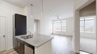 Located at 1100 South Boulevard in Charlotte's vibrant South End neighborhood, this two-bedroom, two-bathroom residence offers a well-designed single-floor layout with standout architectural details throughout. The open-concept living, dining, and kitchen area is anchored by impressively high ceilings that amplify the sense of space. The kitchen features a curved granite-topped peninsula with an undermount sink, dark espresso cabinetry, stainless steel appliances including a refrigerator and range, subway tile backsplash, and stylish pendant lighting. Wood-look plank flooring runs throughout the main living areas, complementing the clean, neutral color palette. Large windows in the living room and primary bedroom frame city skyline views and flood the interior with natural light, each accented by ceiling fans. The primary bedroom includes an en-suite bathroom with dark vanity cabinetry, granite countertops, and a glass-enclosed shower. The secondary bedroom features plush carpeting and its own city-facing window. Three closets provide ample storage, including a walk-in closet with wire shelving. A dedicated laundry area with an in-unit washer adds everyday convenience. The hallway connects all rooms efficiently, completing this thoughtfully laid-out urban residence.