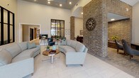 This upscale single-floor clubhouse is thoughtfully designed to offer residents a refined and welcoming communal experience. The space is defined by its soaring ceilings, striking black steel-framed glass partitions, and elegant herringbone-patterned hardwood flooring that flows seamlessly throughout the main gathering areas. Natural light pours in through oversized black-framed windows, offering views of the outdoor pool and surrounding courtyard, creating a bright and airy ambiance.

The main lounge area features plush seating arrangements accented by a modern chandelier and a decorative fireplace, while a rustic sliding barn door adds a warm, contrasting design element. A dedicated meeting or dining area showcases a glass-top table beneath a contemporary globe pendant light, with direct access to the outdoor terrace through double glass doors. Exposed brick archways lend architectural character and a nod to classic craftsmanship.

A well-appointed kitchenette serves as a social hub, complete with granite countertops, dark cabinetry, a coffee station, wine refrigerator, and herringbone tile backsplash. The billiards room provides a spacious recreational retreat with tall windows and a full-size pool table. Private office spaces enclosed by steel-and-glass walls round out this thoughtfully curated amenity space.