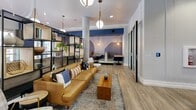This 820 square foot space in Tucson, Arizona, showcases a contemporary open-concept design that maximizes functionality and style. The interior features a harmonious blend of materials, with wood-look flooring throughout and a mix of concrete columns and white walls creating visual interest.

The main area boasts a versatile layout, incorporating a lounge space with a comfortable tan leather sofa, a wooden coffee table, and a patterned area rug. Adjacent to this, a dining section offers booth-style seating with upholstered benches and wooden tables, illuminated by modern globe pendant lights.

A standout feature is the multi-functional shelving unit that serves as a room divider, providing both storage and display space. The kitchenette area is sleek and minimalist, with white cabinetry, stainless steel appliances, and a unique tiled backsplash featuring a playful "ELECTRIFY" text design.

The space is bathed in natural light from large windows, complemented by a variety of lighting fixtures including recessed lights and decorative pendants. Touches of greenery in the form of potted plants add a natural element to the contemporary setting.

Overall, this space combines modern aesthetics with practical design, creating an inviting atmosphere suitable for both work and relaxation in a compact urban environment.