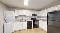 This single-floor residence offers a clean, modern aesthetic with consistent finishes throughout. The kitchen serves as a functional centerpiece, featuring crisp white shaker-style cabinetry with brushed nickel hardware, granite-patterned countertops, and black appliances including a range with overhead ventilation, a dishwasher, and a full-size refrigerator. Light wood-style flooring runs seamlessly through the kitchen and into the living areas, enhancing the sense of continuity and warmth across the space.

The living areas are generously proportioned, with neutral gray walls, clean white baseboards, and ceiling fans with integrated lighting that provide both comfort and illumination. One room features a window fitted with white blinds, allowing natural light to filter in while maintaining privacy.

The bathroom is well-designed, offering a full tub and shower combination with a curved curtain rod, a white vanity with granite-patterned countertop and single basin sink, and matching brushed nickel fixtures and hardware. Wood-style flooring continues here, creating a cohesive look with the rest of the home.

Overall, the space presents a refreshed, move-in-ready interior with a neutral palette and modern finishes that provide a versatile and comfortable living environment.
