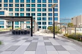 Located at 800 Harbor Blvd in Weehawken, New Jersey, this meticulously designed outdoor terrace offers an impressive amenity space framed by modern high-rise buildings with sleek glass and stone facades. The terrace is defined by expansive stretches of lush, manicured lawn that provide open, flexible gathering space throughout. Wide, large-format stone-paved walkways wind through the grounds, connecting distinct zones and offering easy circulation across the entire level.

Thoughtfully curated landscaping features a variety of ornamental grasses, low shrubs, hedgerows, and seasonal plantings that add texture and greenery throughout. Multiple seating areas are distributed across the terrace, including casual lounge arrangements with wicker furniture and aqua-toned cushions, as well as café-style table and chair sets positioned on the lawn and paved areas, ideal for outdoor dining or socializing.

String lights are strung overhead in certain zones, contributing to an inviting ambiance during evening hours. Sleek, modern light poles are installed throughout, ensuring the space is well-lit after dark. Glass railings along the terrace perimeter provide unobstructed views of the surrounding Weehawken and Hudson River waterfront skyline. The open sky and abundant natural light enhance the overall sense of openness, making this terrace a well-appointed, resort-style outdoor retreat.