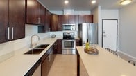 This thoughtfully designed single-floor residence offers a cohesive blend of modern finishes and functional living spaces. The kitchen is a standout area, featuring rich dark-wood cabinetry, light quartz-style countertops, a classic white subway tile backsplash, and a full suite of stainless steel appliances including a range, microwave, and French door refrigerator. A center island provides additional prep and casual dining space, while light wood-style flooring and recessed lighting give the kitchen a clean, contemporary feel. An open layout allows the kitchen to connect naturally to the surrounding living areas.

The primary bedroom is a serene retreat finished with plush carpeting and a large window that invites natural light. It is complemented by a well-organized walk-in closet outfitted with white wire shelving systems offering ample hanging and storage capacity. The primary bathroom features a dark-wood vanity with a white countertop, a framed mirror, and a tub-shower combination with a decorative curtain.

A secondary bathroom mirrors the same refined aesthetic with a matching dark-wood vanity, bright vanity lighting, and adjacent wire shelving for added convenience. A versatile flex room with carpet and a wide window functions as an ideal home office or study. Neutral tones and consistent finishes throughout the space create a warm, inviting atmosphere.