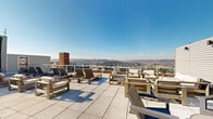Located at 203 W Fourth St in the heart of downtown Cincinnati, this expansive rooftop terrace offers an impressive outdoor retreat above the city skyline. The open-air deck is finished with large-format light-toned pavers that lend a clean, modern aesthetic throughout the space.

The terrace is thoughtfully divided into several distinct zones. A generously sized sun lounging area features multiple chaise lounges and rounded daybeds, ideal for relaxing under the open sky. Numerous seating clusters, composed of teak-framed and dark metal-framed sofas and armchairs with neutral cushions, provide comfortable options for both casual conversation and social gatherings.

A pergola-covered section anchors one end of the rooftop, strung with ambient string lights and accompanied by picnic-style dining tables, creating a shaded area well-suited for outdoor dining and entertaining. A vertical garden wall of lush greenery adds a natural contrast to the urban setting.

Glass-panel railings along the perimeter preserve unobstructed, sweeping panoramic views of the Cincinnati skyline and the rolling hills beyond, visible in every direction. The abundance of natural light throughout the day makes this rooftop an inviting and versatile outdoor space for a wide range of activities.