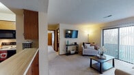 This single-floor residence offers a thoughtfully arranged layout that balances comfort and functionality throughout. The carpeted living room serves as the heart of the home, featuring a wall-mounted flat-screen TV, a sliding glass door that fills the space with natural light, and access to an outdoor balcony. The open feel of the living area flows naturally into the adjacent dining nook, which is anchored by an elegant chandelier and framed by warm, neutral tones. The galley-style kitchen is well-equipped with warm wood cabinetry, generous counter space, a full suite of appliances including a refrigerator, electric range, and built-in microwave, and durable tile flooring. Two bedrooms provide comfortable retreats, each featuring plush carpeting, natural light from windows with blinds, and closet storage. The primary bedroom offers generous proportions with room for a full dresser and additional furnishings. The second bedroom includes a reach-in closet with mirrored doors, adding a sense of depth to the space. A textured ceiling is consistent throughout the unit, lending a classic residential character. The overall ambiance is warm and inviting, with a practical layout well-suited for everyday living.