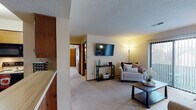 This single-floor residence offers a thoughtfully arranged layout that balances comfort and functionality throughout. The carpeted living room serves as the heart of the home, featuring a wall-mounted flat-screen TV, a sliding glass door that fills the space with natural light, and access to an outdoor balcony. The open feel of the living area flows naturally into the adjacent dining nook, which is anchored by an elegant chandelier and framed by warm, neutral tones. The galley-style kitchen is well-equipped with warm wood cabinetry, generous counter space, a full suite of appliances including a refrigerator, electric range, and built-in microwave, and durable tile flooring. Two bedrooms provide comfortable retreats, each featuring plush carpeting, natural light from windows with blinds, and closet storage. The primary bedroom offers generous proportions with room for a full dresser and additional furnishings. The second bedroom includes a reach-in closet with mirrored doors, adding a sense of depth to the space. A textured ceiling is consistent throughout the unit, lending a classic residential character. The overall ambiance is warm and inviting, with a practical layout well-suited for everyday living.