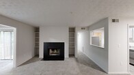 This single-floor, one-bedroom, one-bathroom residence offers a thoughtfully laid-out floor plan across a comfortable footprint. The open living room serves as the centerpiece of the home, anchored by a striking black-tiled wood-burning fireplace flanked by built-in shelving units on either side. A large window with shutters fills the living area with natural light and provides views of the surrounding greenery. Plush carpeting throughout the living spaces adds warmth and comfort underfoot.

The galley-style kitchen is well-equipped with light gray shaker cabinets, granite countertops, a classic white subway tile backsplash, and stainless steel appliances including a refrigerator, range, and dishwasher. Light wood-tone flooring and a pass-through window connecting to the living area enhance the kitchen's bright and functional character.

The primary bedroom is a comfortable retreat, featuring carpet flooring, a window with outdoor views, and easy access to a dedicated walk-in closet outfitted with wire shelving and hanging rods for generous storage capacity. The full bathroom is clean and modern, offering a full-size soaking tub and shower combo, a granite-topped vanity, and crisp white finishes throughout. A hallway connects all rooms efficiently, completing this practical and well-designed residence.