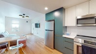 This single-floor unit in Berkeley, CA is designed with a clean, modern aesthetic highlighted by light hardwood flooring and crisp white walls throughout. The open kitchen is a standout feature, showcasing two-tone cabinetry in teal and white, stainless steel appliances including a refrigerator, electric range, and over-the-range microwave, along with white countertops and gold-toned hardware accents. The kitchen flows naturally into the living area, which is bright and airy, benefiting from multiple windows that bring in natural light and offer neighborhood views. A modern multi-bulb ceiling fixture adds a contemporary touch to the living space.

The unit includes multiple bedrooms, each outfitted with platform beds featuring built-in storage drawers, hardwood floors, and windows with blinds. Ceiling fans provide additional comfort. One bedroom accommodates two twin beds with a shared nightstand, while another features a single bed alongside a work desk setup, making it well-suited for study or remote work.

The bathroom is thoughtfully designed with dual vanities featuring teal cabinetry and mirrors, black-and-white penny tile flooring, and a separate walk-in shower with brass fixtures—combining practical functionality with refined design details.