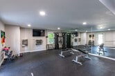 Located at 3307 Leafstone Dr in Covington, GA, this single-level fitness facility is thoughtfully designed to support a comprehensive workout experience. The space is divided into distinct functional zones, each finished with durable rubber flooring that provides both safety and comfort during exercise.

The cardio area features a teal accent wall as a visual anchor and is equipped with a treadmill, elliptical machine, and recumbent bike, along with a wall-mounted fan to ensure proper airflow. Recessed lighting illuminates the space, and a window allows natural light to supplement the interior lighting.

The strength and multi-purpose training zone is finished with neutral white walls and includes a large wall-mounted flat-screen television, wall-mounted yoga mat storage, and a built-in water fountain for convenience. A multi-functional cable machine and a mirrored wall that extends across one full side of the room enhance the space, visually expanding the area and supporting form monitoring. A weight bench and dumbbell rack round out the strength training offerings.

Together, the zones create a clean, organized, and fully functional fitness environment suited for diverse training needs.