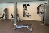 This single-level fitness center is thoughtfully divided into two distinct functional zones. The main cardio and strength training area features durable rubber-textured flooring and is outfitted with multiple treadmills, stationary bikes, ellipticals, and a cable weight machine. A full dumbbell rack lines the mirrored wall, offering a comprehensive range of free weights. Wall-mounted flat-screen televisions are positioned throughout for entertainment during workouts. Large windows along one wall provide an abundance of natural light and direct views of an outdoor pool area and surrounding landscaping, creating an energizing atmosphere. Recessed lighting and stylish pendant fixtures illuminate the space evenly.

Adjacent to the main gym floor is a dedicated studio or flex space, finished with smooth hardwood-style flooring and floor-to-ceiling mirrors that visually expand the room. This area is well-suited for stretching, yoga, or group fitness activities, and is stocked with an assortment of stability balls and foam rollers. Clean white walls, recessed lighting, and a decorative ceiling fixture contribute to a bright, open ambiance. Multiple interior doors provide access to additional areas of the facility, completing this versatile fitness environment.