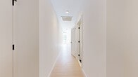 This contemporary single-floor residence is defined by clean lines, a bright neutral palette, and high-quality finishes throughout. Light wood plank flooring runs continuously across the living areas and bedrooms, lending warmth and cohesion to the space.

The open-concept living area is a standout, featuring dramatic floor-to-ceiling black-framed windows that flood the interior with natural light and frame expansive urban skyline views. Exposed concrete columns add an industrial architectural accent that complements the minimalist aesthetic.

The modern kitchen is well-appointed with sleek flat-front cabinetry in warm taupe and white tones, a white tile backsplash, stainless steel appliances including a refrigerator, range, and microwave, and a central island with an undermount sink and matte black faucet — ideal for both cooking and casual dining.

The bedrooms are bright and airy, with crisp white walls and generous proportions. A louvered closet door adds a functional detail in the hallway, which is illuminated by recessed ceiling lighting.

Two bathrooms feature consistent modern finishes: grid-pattern tile floors in slate gray, white subway tile surrounds, light wood vanities with white countertops, backlit mirrors, and matte black hardware and fixtures. One bathroom offers a walk-in glass-enclosed shower, while the other includes a full soaking tub.