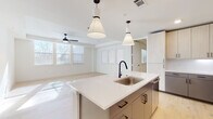 This single-floor space showcases a thoughtfully designed open-concept layout, seamlessly connecting the kitchen and living areas. Light wood flooring runs throughout, creating a warm, cohesive aesthetic that complements the crisp white walls and clean modern finishes.

The kitchen serves as the centerpiece of the space, anchored by a large island with a white quartz countertop, an undermount stainless steel sink, and a matte black faucet. Two stylish pendant lights hang above the island, adding visual interest. The surrounding cabinetry features a two-tone design, pairing light wood upper cabinets with grey lower cabinets and black hardware. A white subway tile backsplash, stainless steel appliances—including a gas range, microwave, and French door refrigerator—complete the functional and stylish kitchen.

The living area is generously proportioned, bathed in natural light from multiple windows, and equipped with a ceiling fan. Tray ceiling detailing adds architectural character to the space.

The bedrooms are well-sized, each featuring ceiling fans and ample natural light. One bathroom includes a marble-tiled walk-in shower with matte black fixtures and an adjacent walk-in closet with built-in shelving, while a secondary bathroom offers a tub-shower combination and neutral tile flooring.