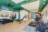 Located at 112 Point Place in Mooresville, NC, this dedicated fitness center offers a thoughtfully designed exercise space across a single floor. The interior is defined by striking tray ceilings accented in a bold teal color, recessed linear lighting, and large ceiling fans that contribute to a bright and energetic atmosphere. Light wood-look flooring and neutral carpet zones divide the space functionally, providing both comfort and practicality underfoot.

The exercise room is generously proportioned and comprehensively outfitted. A full array of cardio equipment, including multiple treadmills and a stationary bike, lines one side of the room alongside windows fitted with slatted blinds that allow natural light while maintaining privacy. The strength training area features a well-stocked freeweight selection with dumbbells and kettlebells, medicine balls, stability balls, a heavy punching bag, and a variety of cable and resistance machines. Wall-mounted mirrors enhance the sense of openness and allow users to monitor their form throughout their workout. Mounted flat-screen televisions add an entertainment element to the cardio zone.

A standout architectural feature is the full-height glass panel garage door that opens directly to an outdoor turf training area, seamlessly connecting the indoor and outdoor fitness environments. A separate adjoining room provides additional space for more focused or private training sessions, completing this versatile and modern fitness facility.