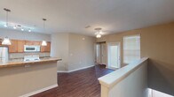 Located at 1205 Springtime Blvd SW in Huntsville, Alabama, this single-story residence offers a well-organized, open-concept layout finished with neutral tones throughout. The living area features rich, dark hardwood-style flooring and is illuminated by a ceiling fan light fixture, creating a bright and functional space. A large window with horizontal blinds allows ample natural light to fill the room, while a half-wall partition defines the boundary between the living area and kitchen without sacrificing the open feel.

The kitchen is equipped with warm-toned wood cabinetry, granite-look countertops, white appliances including a range, microwave, and refrigerator, and a built-in wine rack above the upper cabinets. A peninsula with a sink and pendant lighting provides additional workspace and casual seating potential. Track lighting above adds focused illumination to the cooking area.

The bedrooms are carpeted for comfort and include ceiling fans and closets. One bedroom features a standard closet, while another offers a double-door closet. The bathrooms are finished with hardwood-style flooring, rich wood vanities, granite-look countertops, and vanity lighting. The primary bathroom includes a walk-in shower with sliding glass doors, while the secondary bathroom offers a single vanity and toilet.