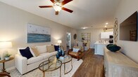This thoughtfully designed single-floor residence offers a seamless open-concept layout that connects the living, dining, and kitchen areas into one cohesive, light-filled space. The living room features rich wood-look flooring, neutral gray walls, large windows with layered blinds and curtains, and a ceiling fan that enhances the airy ambiance. A wall-mounted TV and glass-top coffee table anchor the space alongside a mix of woven and upholstered seating.

The kitchen is well-equipped with white shaker cabinetry, white quartz countertops, a classic subway tile backsplash, and a full suite of stainless steel appliances including a refrigerator, range, microwave, and dishwasher. A peninsula counter provides additional prep space and connects to the dining area.

The bedrooms continue the warm, neutral palette with wood-look flooring and ceiling fans. The primary bedroom offers generous proportions, flanking nightstands, and ample natural light. A secondary bedroom provides a calm, functional retreat with its own window and closet access.

The bathroom is clean and modern, featuring white cabinetry with quartz countertops, a walk-in shower with tile surround, and wood-look flooring that ties the space together cohesively throughout the unit.