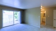 This single-floor residence offers a clean, functional layout designed for comfortable everyday living. The main living area is generously proportioned, featuring soft wall-to-wall carpeting that adds warmth underfoot. A large sliding glass door floods the room with natural light and provides direct access to a private balcony, offering pleasant outdoor views of surrounding greenery. The neutral, muted wall tones throughout the space create a calm and versatile backdrop, making it easy to personalize with furnishings and décor. Flush-mount ceiling lighting provides consistent illumination across the room, complementing the natural light from the balcony door. Just off the main living area, a bathroom is visible and features built-in cabinetry with ample storage, light-toned finishes, and a well-organized vanity area. The open sightlines between rooms contribute to an airy, connected feel throughout the space. The overall ambiance is understated and practical, with a bright, welcoming character driven by the abundance of natural light and the cohesive use of neutral finishes. This space is well-suited for those seeking a straightforward, move-in-ready residence with a comfortable and uncluttered living environment.