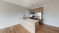 This single-floor unit showcases a contemporary design with a neutral color palette and wood-look luxury vinyl plank flooring that flows consistently throughout the space. The open-concept layout connects the kitchen and living area seamlessly, creating a spacious and functional environment.

The kitchen serves as the focal point, anchored by a generously sized island featuring a light quartz countertop, an undermount sink, and a matte black faucet. Medium-toned wood cabinetry with black hardware lines the walls, complemented by a white subway tile backsplash. Stainless steel appliances — including a refrigerator, range, microwave, and dishwasher — complete the kitchen suite.

The open living area offers ample space with recessed lighting overhead and large sliding glass doors that invite natural light and provide access to a balcony. The bedroom area features neutral gray walls, recessed lighting, and multiple doorways leading to closets and additional rooms.

The bathroom includes a full tub-and-shower combo with white surround panels and coordinating matte black fixtures. A dedicated laundry room houses a full-sized top-load washer and dryer, adding everyday convenience to this well-appointed unit.