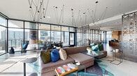 Located at 808 Crawford St in Houston, TX, this striking single-floor living space showcases a seamless blend of contemporary design and curated artistry. The expansive living area is defined by dramatic floor-to-ceiling glass walls on multiple sides, flooding the interior with abundant natural light while offering panoramic views of the Houston skyline and surrounding cityscape.

The space is thoughtfully divided into distinct zones through the use of ornate lattice-patterned screen partitions, which add both visual interest and a sense of intimacy without sacrificing openness. Dark hardwood flooring grounds one section of the space, while a vivid teal-toned area rug anchors the main lounge seating area, where oversized sectional sofas adorned with colorful accent pillows invite relaxed gathering.

A striking sculptural art piece commands attention near the entrance, reinforcing the space's gallery-like quality. Warm wood slat wall paneling with integrated shelving and mounted displays adds texture and warmth to one end of the room, contrasting beautifully with the crisp white ceilings above.

An elaborate pendant lighting installation — featuring dozens of individually suspended lights — creates a dynamic, almost kinetic ceiling feature throughout the main lounge. Direct access to an outdoor terrace further extends the living space, seamlessly connecting interior comfort with outdoor urban views.