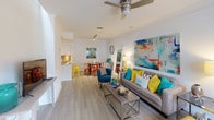 This two-floor residence offers a thoughtfully designed open-concept layout that seamlessly connects the living, dining, and kitchen areas on the main level. The living room is bright and inviting, featuring light wood-style flooring, a ceiling fan, and large windows fitted with blinds that allow generous natural light to fill the space. Bold, colorful abstract artwork anchors the walls, complementing the vibrant teal, yellow, and orange accent pieces throughout.

The kitchen is well-appointed with sleek white gloss cabinetry, granite-style speckled countertops, a gray subway tile backsplash, stainless steel appliances including a refrigerator, electric range, microwave, and dishwasher, plus a deep undermount sink. Track lighting overhead provides excellent task illumination. A dining area adjacent to the kitchen accommodates everyday meals comfortably.

The bedrooms are carpeted for comfort, each equipped with a ceiling fan and ample wall space. One bedroom features direct access to an outdoor balcony. The bathrooms include tiled tub-shower combinations, granite-topped vanities, and wood-style flooring, offering a clean, functional finish consistent with the rest of the residence.