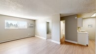 Located at 1869 Coronado Pkwy N in Denver, CO, this one-bedroom, one-bathroom unit offers a practical and efficiently designed single-floor layout. The living room features light wood-style laminate flooring, neutral gray walls, a textured ceiling, and a window-mounted air conditioning unit alongside baseboard heating, ensuring year-round climate control. Natural light enters through horizontal-blind-fitted windows that frame views of surrounding greenery. The open flow from the living area leads directly to the galley-style kitchen, which is outfitted with white cabinetry, marble-look countertops, a stainless steel sink, and stainless steel appliances including a refrigerator and range. The bedroom is carpeted for added comfort and warmth, with a window allowing in natural light and a baseboard heater along the wall. A sliding door closet provides convenient storage. The bathroom features a full tub-shower combination with clean white subway tile surround and chrome fixtures. Throughout the unit, a consistent neutral color palette and clean finishes create a cohesive, move-in-ready atmosphere suited for straightforward, comfortable everyday living.