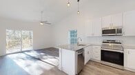 Located at 51 Hillside Rd in Pine Plains, NY, this two-floor home presents a clean, modern aesthetic defined by bright white walls, hardwood-style flooring, and thoughtfully designed living spaces throughout. The open-concept kitchen serves as a central hub of the main level, featuring white shaker cabinetry, granite countertops, a central island with an integrated sink and dishwasher, and a full suite of stainless steel appliances. Pendant lighting with a geometric design hangs above the island, complementing the soaring vaulted ceiling that extends into the adjacent living area. A ceiling fan enhances the airy feel of this space, while sliding glass doors open directly onto a private deck with wooded views, flooding the interior with natural light. The hallway connecting the bedrooms features tall ceilings and a stylish pendant fixture, lending the corridor a refined character. Bedrooms are well-proportioned with vaulted ceilings, ceiling fans, and generous walk-in closets equipped with wire shelving systems. A bathroom showcases marble-style tile flooring, a matching tub surround, and a granite-topped vanity. An attached garage with an automatic opener provides convenient parking and storage. The unfinished basement offers significant potential for future customization.