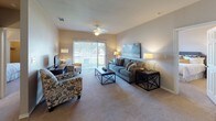 This single-floor community clubhouse offers a thoughtfully designed gathering space with a warm, welcoming ambiance throughout. The main lounge serves as the centerpiece of the facility, featuring a striking stone fireplace framed by elegant white columns and crown molding. Comfortable leather seating and classic wood furnishings create an inviting atmosphere, while arched windows and French doors allow generous natural light to fill the room.

Adjacent to the lounge is a dedicated game room, highlighted by a full-size billiards table positioned beneath a pendant light fixture. Tall arched windows overlook lush outdoor greenery, and a wall-mounted television adds to the recreational appeal. A separate business center, enclosed by glass-paneled French doors, provides multiple computer workstations for residents.

The fully equipped kitchen features rich wood cabinetry, dark granite countertops, tile flooring, and a full suite of appliances including a refrigerator and microwave, making it ideal for hosting community events. Near the entrance, a cozy bistro nook with a high-top table and bar seating, accented by stone tile flooring and transom windows, provides a welcoming transition into the space. Throughout, earthy taupe tones, carpet flooring, and tasteful décor create a cohesive and comfortable community environment.