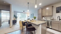This single-story residence is designed with an open-concept layout that seamlessly connects the kitchen, dining, and living areas. The kitchen is outfitted with taupe-toned cabinetry, granite countertops, stainless steel appliances—including a refrigerator and microwave—and a central island with bar seating illuminated by sleek pendant lighting. Wood-style flooring runs throughout the main living areas, adding warmth and continuity.

The living room is generously proportioned, featuring plush carpeting, a ceiling fan, and large sliding glass doors that flood the space with natural light and provide direct access to a private outdoor patio with green views. The open flow between kitchen and living areas makes the layout highly functional.

The bedroom is carpeted and comfortably sized, featuring a ceiling fan and access to a walk-in closet. A full bathroom adjoins the bedroom, offering a dual-sink vanity with granite-style countertops, taupe cabinetry, and a shower with a curved rod. A beverage cooler and additional shelving are also noted in the unit, adding a practical touch. The overall aesthetic is modern and cohesive throughout.