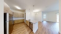 This two-bedroom, two-bathroom residence at 5104 Cherry Hill Rd in Cohoes, NY offers a thoughtfully designed single-floor layout with modern finishes throughout. The open-concept kitchen, dining, and living area forms the heart of the home, featuring warm wood-tone cabinetry, subway tile backsplash, granite countertops, stainless steel appliances including a dishwasher and refrigerator, and a peninsula island with a built-in sink. Pendant lighting and a chandelier above the dining area add an elegant touch, while natural light flows in from the adjoining living room, which is anchored by a large sliding glass door with transom windows offering outdoor views. Durable wood-look flooring runs throughout the main living areas, while the bedrooms feature plush carpeting and bright windows that bring in ample natural light. Both bathrooms are finished with granite-topped white vanities, framed mirrors, and a tub-shower combination. A dedicated in-unit laundry room houses a full-size washer and dryer with overhead shelving for added convenience. A connecting hallway ties all rooms together in a clean, functional flow, creating a comfortable and well-appointed living environment.