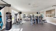 Located at 831 Pecan Ave in Winston-Salem, NC, this fitness center offers a complete exercise facility within a single, well-appointed room. The space is finished with elegant crown molding, warm neutral-toned walls, and recessed lighting that combine to create a polished, welcoming atmosphere. Durable speckled rubber flooring covers the entire area, providing both safety and comfort during workouts.

Large multi-pane windows line the walls, flooding the room with abundant natural light and offering views of the surrounding neighborhood. Ceiling fans ensure consistent airflow throughout the space. Full-length wall mirrors visually expand the room and allow users to monitor their form during exercise.

The cardio section is well-stocked with a row of TRUE-brand treadmills, elliptical trainers, and a stationary cycling bike. The strength-training area features a multi-function cable machine, a selection of selectorized weight machines, and a dedicated free weights station complete with a dumbbell rack, a weight bench, a battle rope, TRX suspension straps, and a punching bag. Wall-mounted flat-screen televisions are positioned throughout for entertainment. A service window is also present, suggesting access to additional amenities nearby.