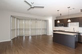 This single-floor space showcases a contemporary open-concept design that seamlessly connects the living and kitchen areas. The living space is anchored by warm hardwood-style flooring and benefits from abundant natural light streaming through a striking bank of floor-to-ceiling windows fitted with roller shades, creating an airy, expansive atmosphere. A ceiling fan provides additional comfort throughout the main living area, which also features sliding glass door access to the outdoors.

The kitchen is thoughtfully appointed with dark espresso cabinetry, granite countertops, a white subway tile backsplash, and a full suite of stainless steel appliances including a refrigerator, dishwasher, built-in microwave, and range. A kitchen island with matching granite provides additional prep and seating space, while pendant lighting adds a refined touch overhead.

The bedroom offers plush carpeting, a ceiling fan with light fixture, and a horizontal window that brings in natural light while maintaining privacy. The bathroom is clean and functional, finished in crisp white tile with a combination tub and shower, chrome fixtures, and simple, understated detailing throughout.