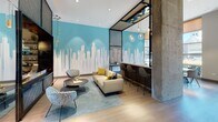 Located at 1630 Chicago Ave in Evanston, Illinois, this single-floor amenity space is a thoughtfully designed community hub that blends contemporary aesthetics with functional, social-oriented areas. The entrance greets visitors with a dramatic lobby featuring soaring floor-to-ceiling glass windows that flood the space with natural light and offer views of the surrounding streetscape. A sleek reception desk framed by warm wood slat paneling and a vibrant cityscape mural sets a welcoming tone.

At the heart of the space is an expansive bar and lounge area anchored by a long white quartz countertop lined with modern bar-height seating. Overhead, a striking slatted wood ceiling with clustered globe pendant lights creates a warm, refined atmosphere. Adjacent lounge seating, including plush sofas and sculptural accent chairs, surrounds a bold teal feature wall adorned with a Chicago skyline mural, adding a locally inspired artistic touch.

A dedicated coworking zone provides workstation seating along communal tables, complemented by exposed concrete columns and an open industrial ceiling that adds urban character. Throughout the space, light wood flooring, teal and yellow accent furnishings, and curated wall art create a cohesive, vibrant design language. The overall ambiance is modern, energetic, and conducive to both work and social interaction.