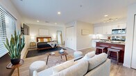 TRELLIS Herndon Unit 1 is a well-appointed studio unit located in Herndon, Virginia, offering a smart and efficient open-concept floor plan on a single level. The main living area seamlessly integrates the sleeping, living, and kitchen spaces, all unified by warm-toned luxury vinyl plank flooring that runs throughout. Natural light filters in through large windows with horizontal blinds, brightening the neutral-toned walls and creating an inviting ambiance.

The kitchen is a standout feature, equipped with stainless steel appliances including a refrigerator, range, microwave, and dishwasher. White shaker cabinetry with gold hardware pairs elegantly with granite countertops and a classic subway tile backsplash. A rich wood-toned breakfast bar with seating provides a casual dining option. Notably, the kitchen also houses an in-unit washer for added convenience.

The open living area provides ample space for both a seating arrangement and a sleeping area, with a double-door closet offering generous storage. Recessed lighting illuminates the space evenly throughout.

The bathroom features tile flooring, a tub-shower combination with tiled surround, and a clean, minimalist finish. This unit offers a functional and stylish living experience in a compact, efficiently designed space.