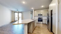 This single-floor residence offers a clean, contemporary design with wood-look flooring, neutral tones, and abundant natural light throughout. The open-concept layout centers around a well-appointed kitchen featuring a large granite-topped island with an integrated sink and dishwasher, stainless steel appliances including a range, microwave, and refrigerator, and crisp white cabinetry complemented by a white subway tile backsplash. The kitchen flows seamlessly into the living area, which is equipped with a ceiling fan and access to a private balcony through glass doors, filling the space with natural light. The bedrooms are bright and well-proportioned, each with wood-look flooring, neutral walls, and windows fitted with horizontal blinds. One bedroom includes a ceiling fan and sliding glass door access to an outdoor area. The primary suite is complemented by a generously sized walk-in closet with multiple hanging rods and built-in shelving for ample storage. The bathroom features a full tub-shower combination with white tile surround, a granite-topped vanity with modern cabinetry, and consistent wood-look flooring. Throughout the residence, five-panel interior doors, recessed lighting, and a cohesive neutral palette contribute to a modern and functional living environment.