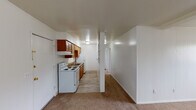 This single-floor unit offers a straightforward and functional layout connecting the kitchen, living area, bedrooms, and bathroom in an efficient flow. The kitchen is outfitted with warm-toned wood cabinetry, laminate countertops, a double-basin sink, a white electric range, and a full-size refrigerator. Wood-look vinyl flooring runs throughout the kitchen, while a galley-style design maximizes storage and counter space along one wall.

The living area is generously proportioned, with neutral carpet, white walls, and a ceiling-mounted light fixture. The kitchen and living space are partially divided by a half-wall, creating a sense of separation while maintaining an open feel. A wall-mounted air conditioning unit and baseboard heaters are present, providing climate control options year-round.

The two bedrooms are carpeted, each featuring white walls, baseboard heating, and windows with exterior views that allow natural light to fill the rooms. Both offer a clean, versatile canvas for furnishing.

The bathroom includes a wide dual-sink vanity with white cabinetry, a large mirror with overhead lighting, wood-look flooring, and a tub-shower combination, providing practical convenience for daily use.