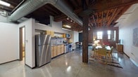 Unit N308 at 2001-19 Washington Ave is a distinctive industrial-style loft in St. Louis, Missouri, showcasing the character of a thoughtfully converted historic building. The single-floor layout embraces an open-plan design where the kitchen, dining, and living areas flow seamlessly together beneath soaring ceilings with exposed wooden beams, ductwork, and timber columns that speak to the building's storied past.

The kitchen is outfitted with stainless steel appliances — including a refrigerator, range, microwave, and dishwasher — paired with light maple cabinetry and a stainless steel countertop and backsplash rail system. Polished concrete floors run throughout, adding to the loft's urban aesthetic. The living area features exposed brick accent walls and arched window openings that bring warmth and texture to the space.

The unit includes multiple sleeping areas: a primary bedroom with a serene, neutrally appointed atmosphere and exposed brick detail, and a secondary sleeping nook enclosed by original brick walls and large windows that bathe the space in natural light. A dedicated workspace sits alongside the living area, and the bathroom provides a full tub-shower combination. In-unit laundry access is also available, adding everyday convenience to this characterful St. Louis loft.