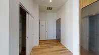 This contemporary single-floor residence showcases a clean, modern design throughout. The open-concept living area is bright and airy, featuring light hardwood-style flooring that flows seamlessly from room to room, creating a cohesive and inviting atmosphere. Soaring ceilings add a generous sense of vertical space, enhancing the overall openness of the layout.

The kitchen is thoughtfully designed with rich walnut-toned cabinetry extending to the ceiling, complemented by light quartz countertops, a white tile backsplash, and stainless steel appliances including a range, built-in microwave, and refrigerator. A peninsula with pendant lighting connects the kitchen to the living space, making it ideal for both everyday living and entertaining.

The bedroom area features a sliding-door closet with open shelving, offering practical built-in storage. A dedicated utility panel is neatly integrated into the space. The bathroom is elegantly finished with large-format grey floor tiles, a soaking tub, and floor-to-ceiling marble-patterned wall tile surrounding the tub surround.

A standout feature of this residence is the corner floor-to-ceiling glass doors that open to a private balcony, flooding the interior with natural light and offering sweeping views of the surrounding cityscape, including palm trees on the horizon.