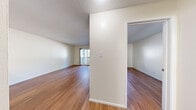 This single-story unit in Walnut Creek, California offers a clean, functional layout with consistent hardwood-style flooring throughout the main living areas. The open living space is bright and airy, benefiting from natural light that streams in through a large sliding glass door leading to a private balcony, as well as an additional window that frames outdoor greenery. A wall-mounted air conditioning unit provides climate control directly within the living area.

The layout is defined by a central dividing wall that separates the living space from an adjoining room, which features mirrored closet doors and its own access to additional areas of the unit. Textured popcorn ceilings are present throughout, adding a characteristic finish to each room.

The kitchen is efficiently designed, featuring white cabinetry, light countertops, and a stainless steel electric range with an overhead ventilation hood. The space offers practical storage through its cabinet configuration and provides a functional cooking environment.

Throughout the unit, crisp white walls create a neutral backdrop, while the warm-toned flooring adds visual continuity. The overall ambiance is clean and move-in ready, offering a straightforward, well-maintained living environment in the 94596 zip code area.