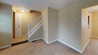 This three-floor residence offers a practical and well-organized layout across its levels. The main living area is finished with neutral-toned carpet and warm beige walls, creating a comfortable atmosphere. Large windows fitted with vertical blinds allow generous natural light to fill the space while offering views of the surrounding greenery. A white-painted staircase with a classic spindle railing connects the floors, adding a traditional architectural touch.

The kitchen is equipped with warm oak cabinetry offering ample storage, white laminate countertops, tile flooring, and recessed lighting overhead. Appliances include a refrigerator, electric cooktop, and dishwasher, all arranged in a galley-style configuration that maximizes functionality.

Multiple bedrooms are carpeted and feature the same neutral palette, each with windows that frame outdoor views of trees and landscaping, providing a calm and private setting.

The bathrooms include a full bath with a white tiled tub-and-shower combination and chrome fixtures, as well as a secondary bathroom with a walk-in shower stall, single-sink vanity with oak cabinetry, and a mirrored medicine cabinet.

The basement level serves as a utility space, featuring exposed wood-beam ceilings, painted concrete floors, support columns, and dedicated areas for laundry and mechanical systems including a water heater and HVAC unit.
