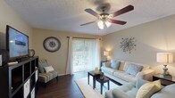 This single-story, one-bedroom, one-bathroom residence is thoughtfully laid out across a comfortable and functional floor plan. Dark hardwood-style flooring flows consistently throughout the main living areas, providing a warm, cohesive aesthetic.

The living room serves as the central gathering space, featuring a ceiling fan with light fixture, neutral-toned walls, and a sliding glass door dressed with vertical blinds and sheer curtains that invite natural light and provide outdoor access. A dedicated dining area adjoins the living space, accommodating a glass-top dining table and chairs beneath a window fitted with blinds and curtains, with a wall mirror adding depth to the room.

The galley-style kitchen is well-equipped with rich wood cabinetry, a tile backsplash, double sink, and black appliances including a refrigerator, range, microwave, and dishwasher. Dark hardwood flooring continues here, complementing the warm cabinetry tones.

The bedroom features a teal accent wall, ceiling fan, hardwood flooring, a large window for natural light, and a closet with built-in storage. The bathroom is finished with cool blue-gray walls and a shower-tub combination. Throughout, textured ceilings and ceiling fans are consistent features of the space.