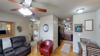 The Arctic Fox is a charming 2-bedroom, 1-bathroom single-floor space designed for comfortable, functional living. The open layout connects the living area, kitchen, and bedrooms in a seamless flow, making the most of the available space.

The living area features warm hardwood-style flooring, a ceiling fan with light fixture, and room for relaxed seating, including a plush leather recliner and a bold red accent chair that adds a pop of color to the neutral palette. Recessed lighting and soft wall tones create a welcoming ambiance throughout.

The kitchen is well-appointed with warm wood cabinetry, a black refrigerator, and a dark dishwasher, complemented by a classic sink setup and ample counter space. Decorative accents above the cabinets add a personalized touch to the cooking area.

The bedroom, visible through an open doorway, offers a cozy retreat with carpeted flooring, a classic bed frame, and a bright window that invites natural light. An adjacent hallway leads to additional rooms and the bathroom, ensuring a practical and easy-to-navigate floor plan.

Overall, The Arctic Fox presents a well-maintained, inviting space with a warm color palette, thoughtful décor, and a layout that balances comfort and functionality for everyday living.