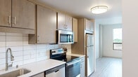 This efficiently designed one-bedroom, one-bathroom unit offers a thoughtful layout across a single floor, making excellent use of every square foot. The kitchen is a standout feature, outfitted with light wood cabinetry, white subway tile backsplash, light quartz countertops, and a full suite of stainless steel appliances including an electric range, over-the-range microwave, dishwasher, and refrigerator. A stainless steel sink with a modern pull-down faucet completes the functional workspace.

Light wood-tone flooring runs throughout the unit, lending a clean, contemporary feel that connects each area seamlessly. The main living area is bright and open, benefiting from large floor-to-ceiling windows and a sliding glass door that opens onto a balcony, offering views of the surrounding landscape and filling the space with natural light.

The generously sized bedroom includes a walk-in closet with built-in shelving, providing ample storage. A sliding barn-style door adds a modern touch to the room's entrance.

The bathroom features a wide vanity with a rectangular undermount sink, quartz countertop, a large wall mirror, and brushed nickel fixtures and grab bars, combining style with practicality. Tile flooring completes the clean, neutral aesthetic of this well-appointed unit.
