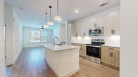 This well-appointed 1-bedroom, 1-bathroom residence offers a thoughtfully designed open-concept layout that maximizes every square foot. Warm wood-look flooring flows continuously throughout the entire space, creating a cohesive and inviting atmosphere.

The kitchen serves as the heart of the home, anchored by a large central island with a granite countertop, an undermount sink, and elegant pendant lighting overhead. Cabinetry combines crisp white upper shaker-style cabinets with natural wood-toned lower cabinets, accented by matte black hardware. Stainless steel appliances, including a range, microwave, and refrigerator, complete the modern kitchen. A built-in desk nook is also conveniently situated nearby. The kitchen opens seamlessly into the living area, which features a ceiling fan and large windows that invite an abundance of natural light.

The bedroom is a comfortable, well-proportioned retreat with a ceiling fan, a window overlooking the surrounding neighborhood, and clean neutral walls. The full bathroom is generously sized, offering a double-sink vanity with granite countertops, framed mirrors, matte black fixtures, ample white cabinetry for storage, and a walk-in glass-enclosed shower. The overall aesthetic is clean, contemporary, and move-in ready.