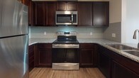 Located at 1411 E 105th St in Cleveland, Ohio, this single-floor unit offers a thoughtfully designed open-concept layout with a cohesive, contemporary aesthetic throughout. Hardwood-style flooring extends across all living areas, providing a warm and consistent foundation that ties each space together.

The kitchen serves as a focal point of the main living area, featuring rich dark cabinetry, granite countertops, and a full suite of stainless steel appliances including an electric range, over-the-range microwave, dishwasher, and refrigerator. A light gray subway tile backsplash adds a modern touch, while pendant lighting suspended above the peninsula illuminates the space and reinforces the open connection to the living area. A large window at the far end of the living space invites natural light, brightening the open floor plan.

The bedroom is generously sized, offering clean white walls and ample room for furnishings. It connects directly to a well-appointed bathroom featuring dual dark wood vanities, each topped with granite countertops and framed by large mirrors. A soaking tub is also present, adding comfort and functionality. The overall design is clean, modern, and move-in ready.