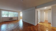 This single-floor residence showcases a consistent design character throughout, anchored by richly toned parquet wood flooring that extends across the living areas and bedrooms. The open living and dining area is generously proportioned, with natural light streaming in through large windows that offer views of surrounding greenery. Baseboard heating and window air conditioning units are present throughout, ensuring year-round comfort. Clean white walls provide a neutral backdrop, lending the space a bright and airy feel.

The galley-style kitchen is efficiently laid out, featuring warm oak cabinetry paired with dark stone-look countertops, a stainless steel gas range, a dishwasher, and an overhead range hood. Light tile flooring in the kitchen contrasts pleasantly with the parquet found in the rest of the residence.

The bedroom is a comfortable, well-lit room with its own window, parquet flooring, and a closet with louvered doors, offering practical storage. Additional louvered closets are found in the hallway area, providing ample storage options throughout.

The bathroom is finished in classic white subway tile surrounding a full soaking tub and shower combination, complemented by white cabinetry and tile flooring, delivering a clean and timeless aesthetic. Overall, the space presents a functional and well-maintained layout with consistent finishes throughout.