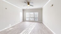 Located at 5500 Oakley Industrial Blvd in South Fulton, GA, this one-bedroom, one-bathroom residence offers a well-organized single-floor layout designed for comfortable everyday living. The combined kitchen and living area serves as the heart of the home, where a peninsula with light quartz-style countertops opens the kitchen to the living space. The kitchen is outfitted with crisp white shaker-style cabinetry, ample storage, a stainless steel refrigerator, and a stainless steel range with an overhead ventilation hood. Light wood-style flooring runs through the main living areas, complementing the neutral warm-gray walls and white trim throughout. The living room benefits from a large multi-panel window that invites abundant natural light, crown molding, and a ceiling fan with a light fixture overhead. A hallway with crown molding detail connects the main living area to the private bedroom, which features soft carpeting, a ceiling fan, a closet with panel doors, and windows providing additional natural light. The bathroom is finished with wood-style vinyl flooring, a white vanity with drawer storage, and clean, neutral walls. A dedicated closet provides additional storage within the unit.