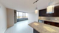 This single-floor apartment at 150 Forest Ave in Oak Park, IL offers a thoughtfully designed living space with a modern aesthetic. The galley-style kitchen is equipped with stainless steel appliances, including a gas range, microwave, and dishwasher, complemented by dark cabinetry, granite countertops, a mosaic tile backsplash, and track lighting. A granite-topped island provides additional prep space. The open living area features light tile flooring and floor-to-ceiling windows that invite abundant natural light and outdoor views. The bedroom includes plush carpeting and a spacious closet, while the bathroom offers a granite vanity and clean tile flooring throughout.