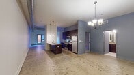 This single-floor unit showcases an industrial-modern design throughout its open layout. Polished concrete floors anchor the main living areas, complemented by exposed silver ductwork running across the ceiling, adding a distinctive loft-like character. A chandelier and pendant lighting illuminate the space with a warm, contemporary feel.

The kitchen is a standout feature, equipped with dark espresso cabinetry, stainless steel appliances including a gas range, built-in microwave, and refrigerator. A peninsula with a light stone countertop and an undermount double sink serves as both a workspace and a casual dining area, with pendant lights hanging above.

The living and dining areas offer an open, flexible layout with generous ceiling height and a sliding door panel that defines the transition between spaces. Natural light enters through a window at the far end of the main area.

The bedrooms are carpeted and notably feature high ceilings and skylights that bring in natural overhead light. Closet space with built-in shelving is present, and each bedroom benefits from a calm, subdued ambiance. The bathrooms include dark vanities with stone-toned countertops, tile flooring, and full tub-shower combinations. A dedicated laundry closet with a stacked washer and dryer provides added convenience.
