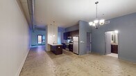 This single-floor unit showcases an industrial-modern design throughout its open layout. Polished concrete floors anchor the main living areas, complemented by exposed silver ductwork running across the ceiling, adding a distinctive loft-like character. A chandelier and pendant lighting illuminate the space with a warm, contemporary feel.

The kitchen is a standout feature, equipped with dark espresso cabinetry, stainless steel appliances including a gas range, built-in microwave, and refrigerator. A peninsula with a light stone countertop and an undermount double sink serves as both a workspace and a casual dining area, with pendant lights hanging above.

The living and dining areas offer an open, flexible layout with generous ceiling height and a sliding door panel that defines the transition between spaces. Natural light enters through a window at the far end of the main area.

The bedrooms are carpeted and notably feature high ceilings and skylights that bring in natural overhead light. Closet space with built-in shelving is present, and each bedroom benefits from a calm, subdued ambiance. The bathrooms include dark vanities with stone-toned countertops, tile flooring, and full tub-shower combinations. A dedicated laundry closet with a stacked washer and dryer provides added convenience.