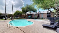 This single-story residence is part of a well-established brick building community set among mature trees, with access to a freeform outdoor pool surrounded by a spacious aggregate deck, seating areas, and lush greenery — offering a resort-like atmosphere for residents.

Inside, the interiors strike a balance between industrial and refined aesthetics. Dark polished concrete floors run throughout, providing a grounded, modern foundation that contrasts beautifully with the warm, neutral-toned walls. Recessed lighting illuminates the space cleanly from above.

The dining area is a standout feature, anchored by a striking round green marble table paired with rattan chairs atop a woven area rug. A large framed abstract artwork adorns the wall, adding a gallery-quality touch to the space. A sliding barn door on a black metal track connects rooms with both function and character.

The unit incorporates thoughtful design details, including a rustic set of antique-style doors that open to a secondary space displaying additional artwork and framed prints. Hallways are clean and minimal, with textured white walls and natural light filtering through. The overall ambiance is curated and eclectic, blending artistic sensibility with comfortable, livable design.