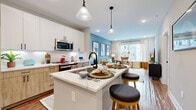 Located at 2010 N Brevard St in Charlotte, NC, this single-floor residence offers a thoughtfully designed open-concept layout with contemporary finishes throughout. The kitchen serves as the heart of the home, featuring a large central island with quartz countertops and bar seating, a full suite of stainless steel appliances, and a stylish mix of white upper cabinetry paired with warm wood-toned lower cabinets. A classic white subway tile backsplash and pendant lighting complete the space. Hardwood flooring flows seamlessly from the kitchen into the living area, where large windows allow abundant natural light and provide views of the surrounding neighborhood. The living room is defined by a muted blue accent wall and an inviting atmosphere well-suited for both relaxing and entertaining. The bedroom continues the bold design aesthetic with a rich teal accent wall, plush carpeting, and generous natural light from a sizable window. The bathroom is clean and modern, finished with large-format tile flooring, a wood-toned vanity, and a glass-enclosed walk-in shower clad in crisp white tile with matte black hardware accents. Every detail of this residence reflects a cohesive, contemporary design sensibility.
